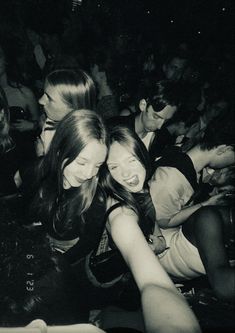 black and white photograph of three girls hugging each other in front of a group of people