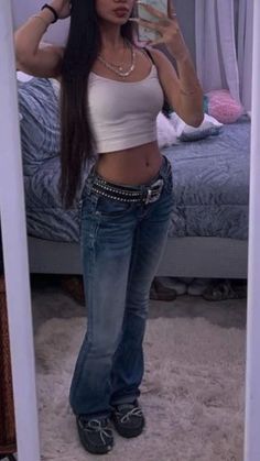 a woman standing in front of a bed wearing jeans