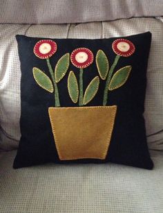 a black pillow with red and green flowers in a pot on the back of a couch