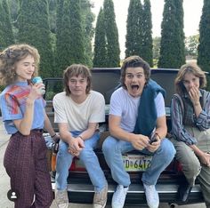 three young people sitting on the back of a pick up truck with their mouths open