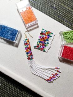 beaded earrings are sitting on a table next to some containers with beads in them