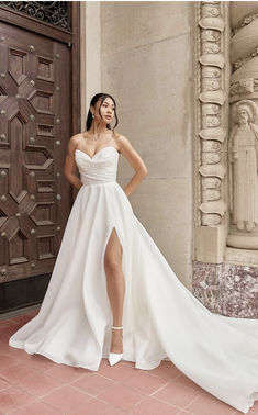 a woman standing in front of a door wearing a white dress with high slits