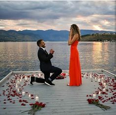 a man kneeling down next to a woman in an orange dress on a dock with candles