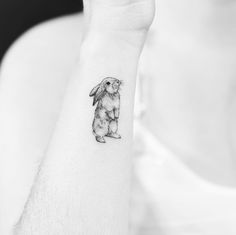 a black and white photo of a small rabbit tattoo on the left inner arm,