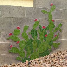 a green cactus painted on the side of a brick wall next to gravel and rocks