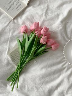 pink tulips are laying on a bed next to an open book