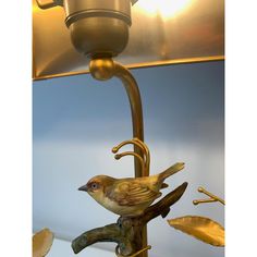 a lamp with a bird on it and leaves around the base that are gold colored