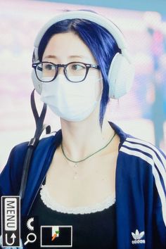 a woman with blue hair wearing headphones and a face mask in front of a tv screen