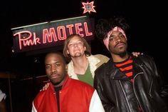 three men standing next to each other in front of a neon sign that reads pink motel