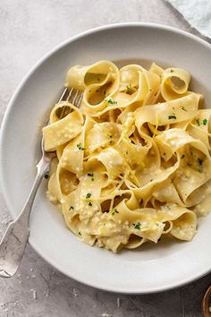 a white bowl filled with pasta and sauce on top of a table next to a fork