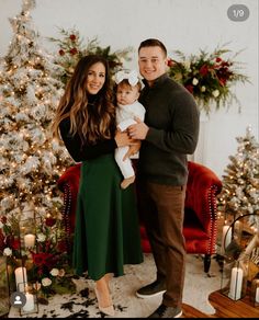 a man and woman holding a baby in front of a christmas tree