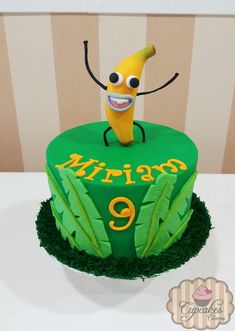 a green cake with a banana on top and the number nine written in yellow icing