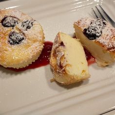 two pastries on a white plate covered in powdered sugar and blueberry sauce