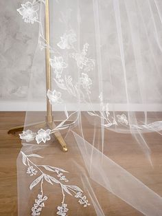 a white veil with flowers on it and a gold stand in front of the curtain