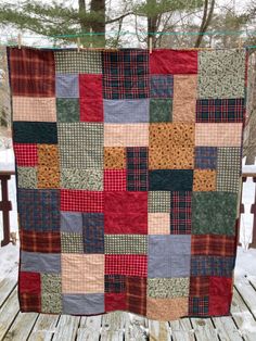 a patchwork quilt hanging on a clothes line in the snow with trees behind it