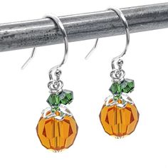 pair of earrings with orange and green glass beads on silver earwires hanging from a metal hook