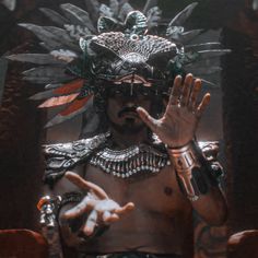 a man in an elaborate headdress holding his hands up