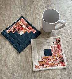 two coasters and a coffee cup on a wooden table with a mug in the middle