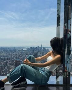 a woman sitting on top of a tall building looking out at the city below her