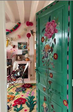 a green door with flowers painted on it in a room filled with furniture and decor