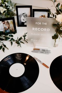 two black records sitting on top of a white table next to flowers and framed pictures