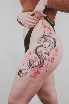 a woman's thigh with a dragon tattoo on the side and flowers around it