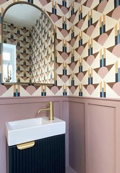 a sink and mirror in a room with wallpaper on the walls, along with a gold faucet