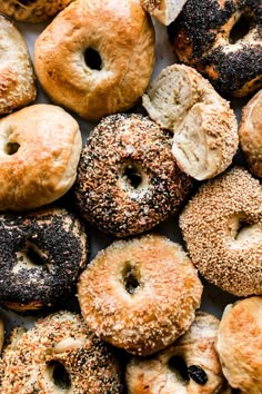 many bagels with different toppings are arranged on a white tablecloth, top view