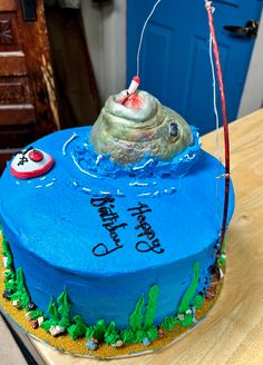 a blue birthday cake with a fishing hook on it's top and happy birthday written on the bottom