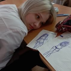 a woman laying on top of a wooden table next to a piece of paper with drawings