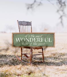 a wooden rocking chair sitting in the middle of a field next to a sign that says, at the most wonderful time of the year