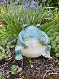 a frog statue sitting on top of a flower pot in the ground next to plants