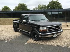 a black pickup truck parked in front of a glass building with trees and grass behind it