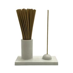 a white vase with sticks in it on top of a table next to a cup