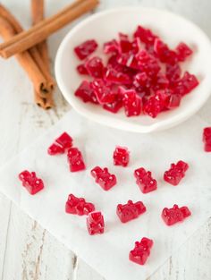 a white bowl filled with red gummy bears next to cinnamon sticks