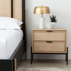 a nightstand with two plants on it next to a bed