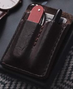 a pocket knife and some watches on top of a black table with a leather case