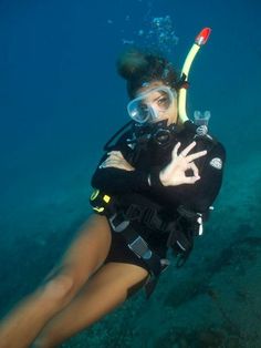 a woman scubas in the water with her hand on her chest and wearing a diving mask