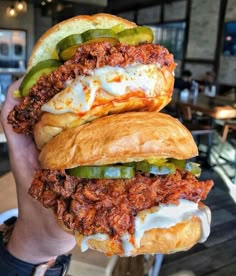 two sandwiches with meat, cheese and pickles are held in front of the camera