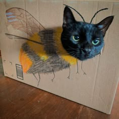 a black cat sitting in a cardboard box with a bee on it's back