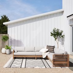 a couch sitting on top of a rug next to a white building and potted plant