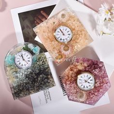 three clocks sitting on top of a magazine next to flowers and rocks in vases