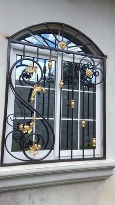 an iron window with gold flowers on the side and bars in the top, along with white walls