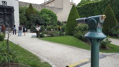 people are walking around an outdoor garden with trees and bushes on either side of the path