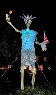 the statue of liberty is lit up at night with an american flag in his hand