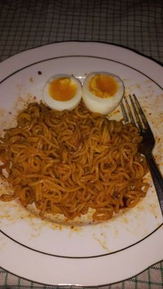 a plate with noodles and two boiled eggs sitting on top of it next to a fork