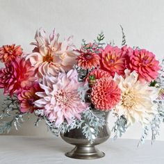 a silver vase filled with lots of pink and white flowers on top of a table