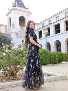 a woman standing in front of a building wearing a black dress with flowers on it