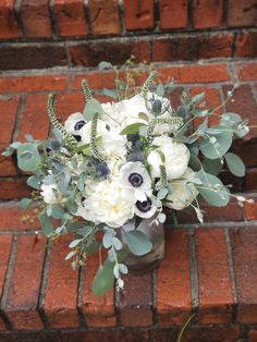 a vase filled with white flowers and greenery on top of a red brick wall