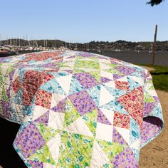 a quilted table cloth sitting on top of a wooden bench next to the water